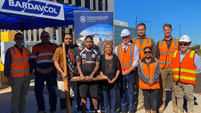 Team members in hi-vis vests stand beside Aunty Rosalind and her sonds. Some team members are wearing hard-hats.